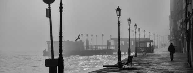 grayscale city water shore with lamp posts and pedestrian