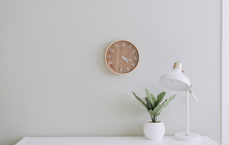 desk with plant and lamp in front of wall with clock